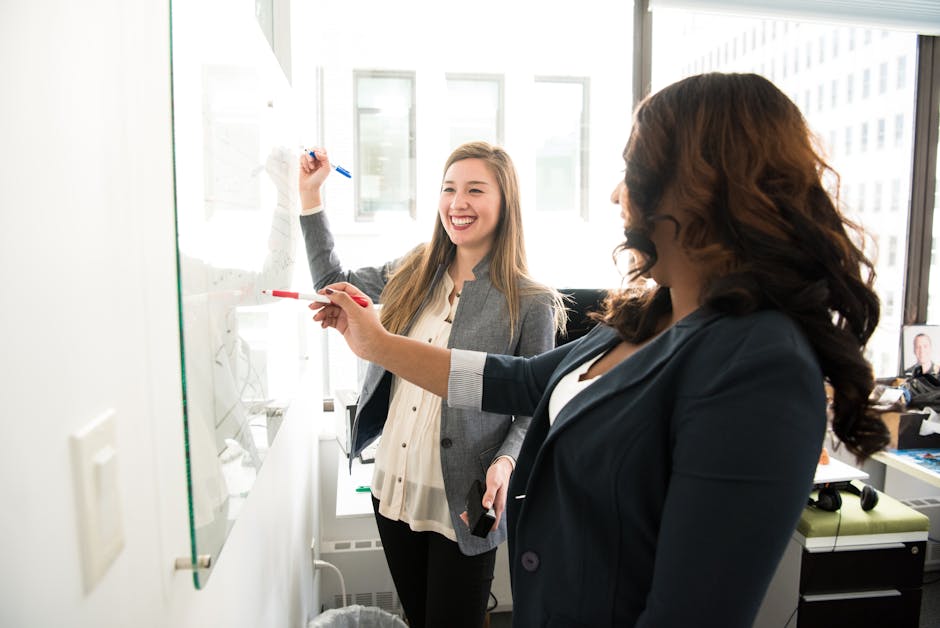 Two professional women discussing ideas on a whiteboard in a modern office setting - showcasing collaborative content creation